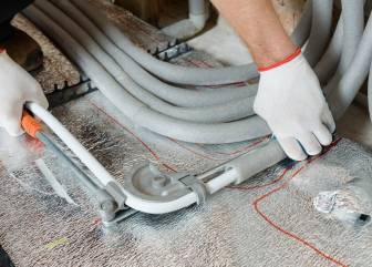 Worker is installing a pipe for the warm floor in the apartment. He is a bend pipe.
